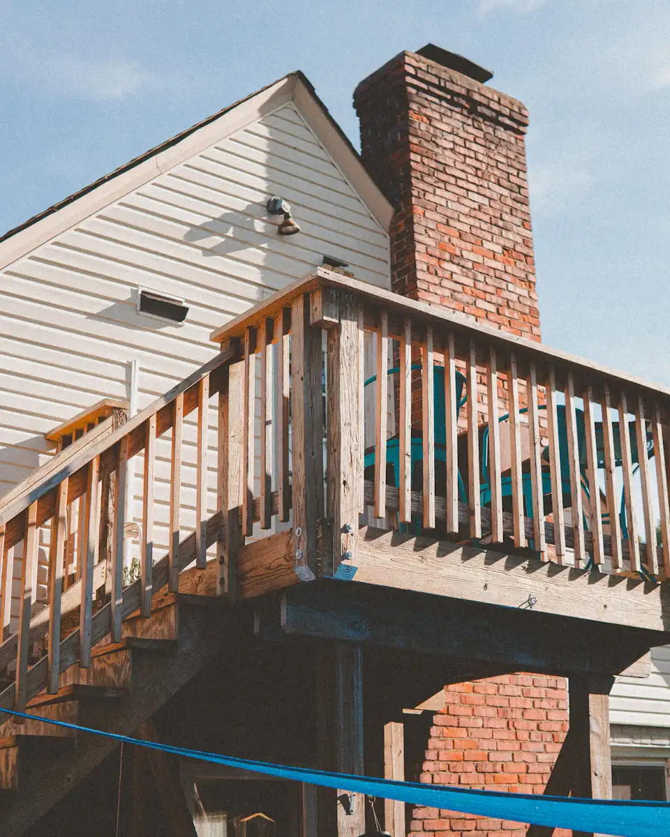 A raised wood deck and stairs at the back of a house with a brick chimney