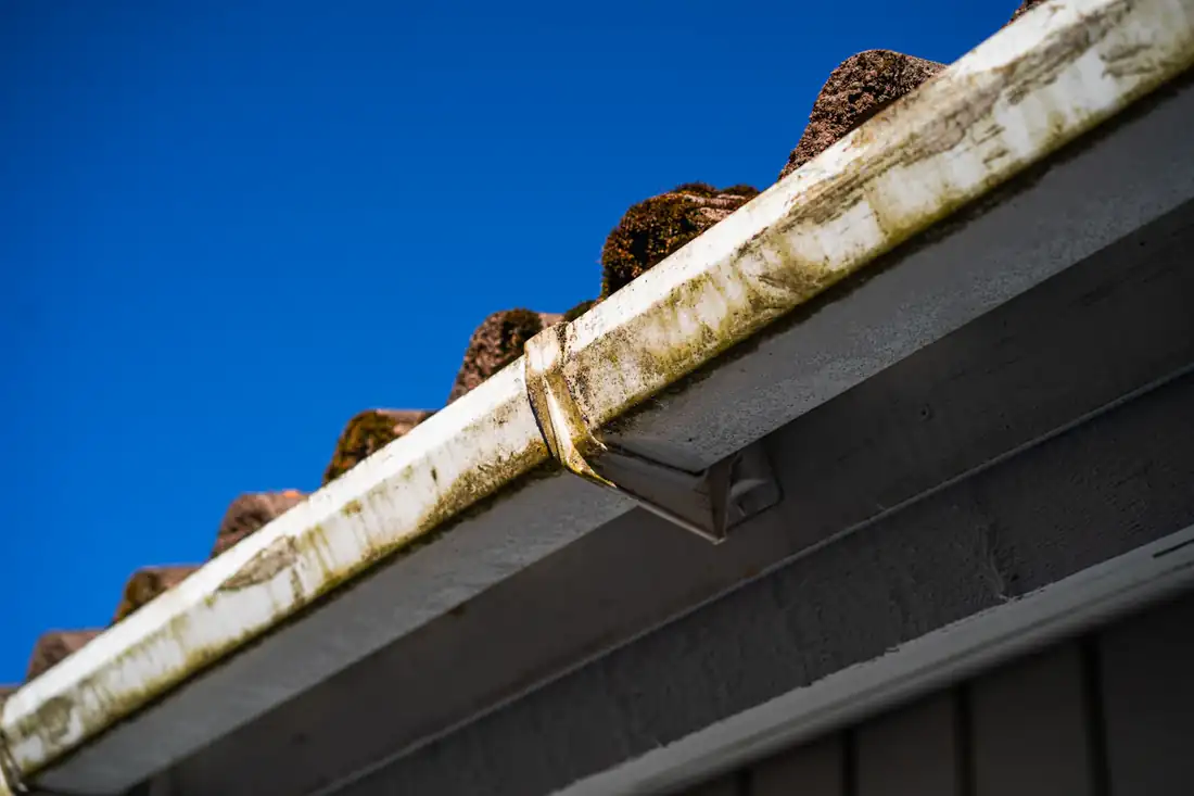 A stained gutter below moss-covered roof tiles
