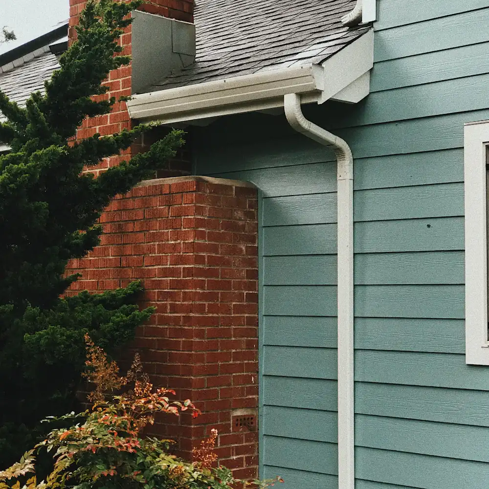 Blue wood siding, a white gutter and downspout, and a red brick chimney