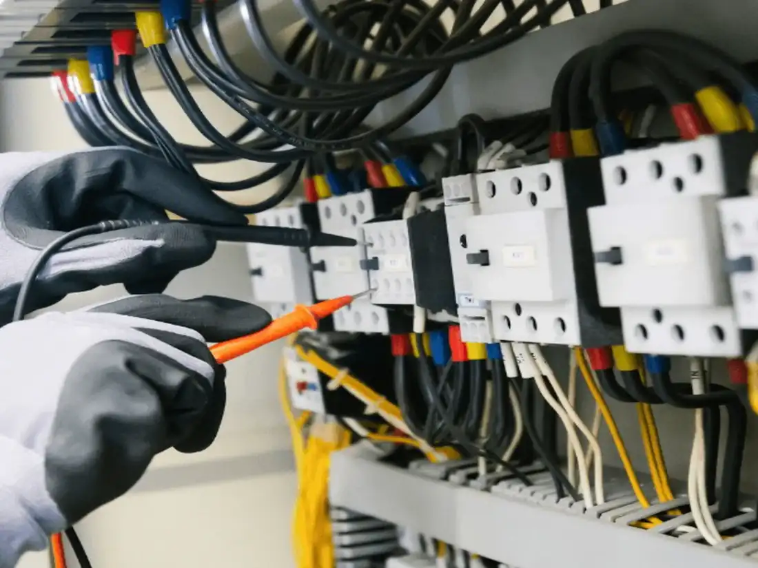 Gloved hands testing wiring in an open electrical panel